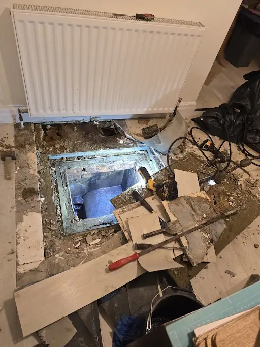 Drainage access opening beneath an indoor floor beside a radiator
