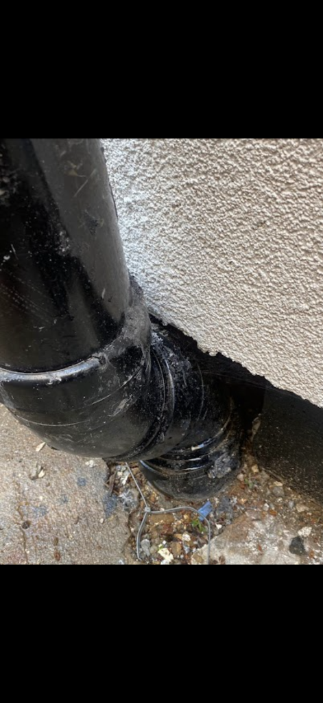 Black external pipe bend and connection beside a wall in Bedford
