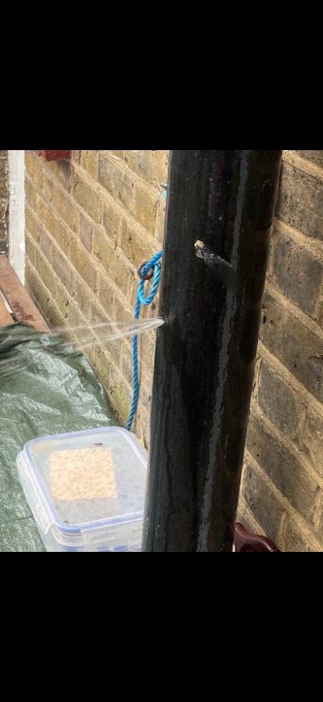 Water discharging from an opening in external black pipework in Bedford