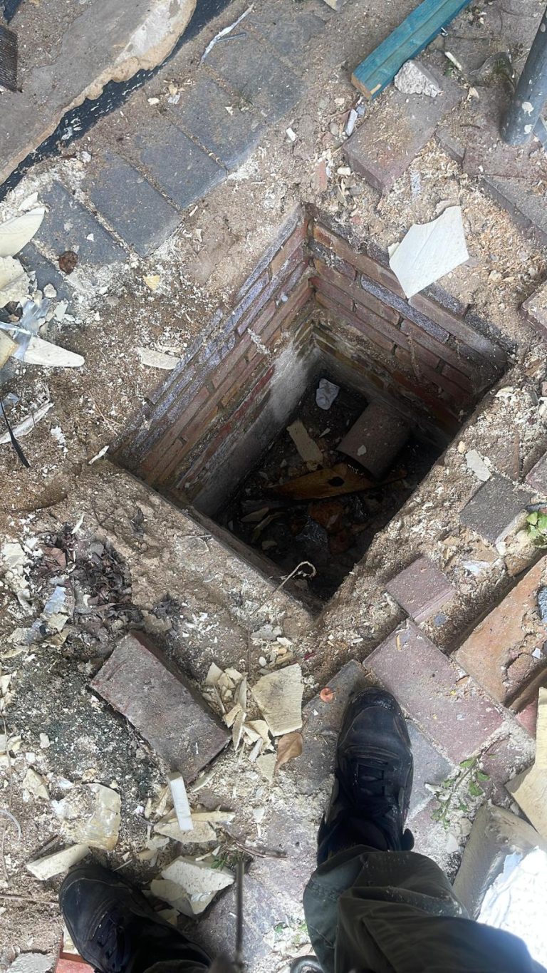 Open brick inspection chamber with debris around the drainage access.