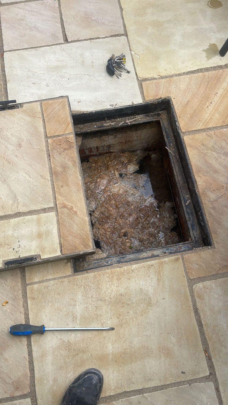 Drainage access in paving with wastewater and accumulated material visible.