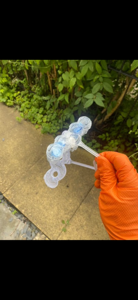 Toilet freshener holder removed from a blocked toilet in Essex, held in an orange glove outdoors